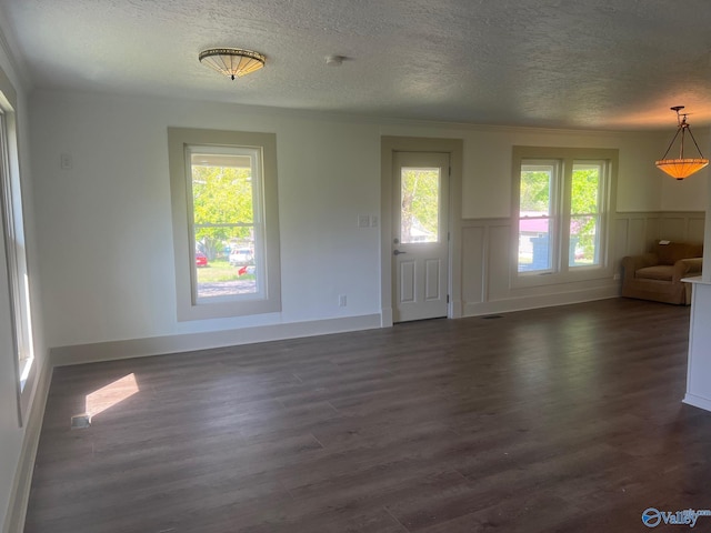 unfurnished living room with wainscoting, ornamental molding, a textured ceiling, and dark wood-style floors