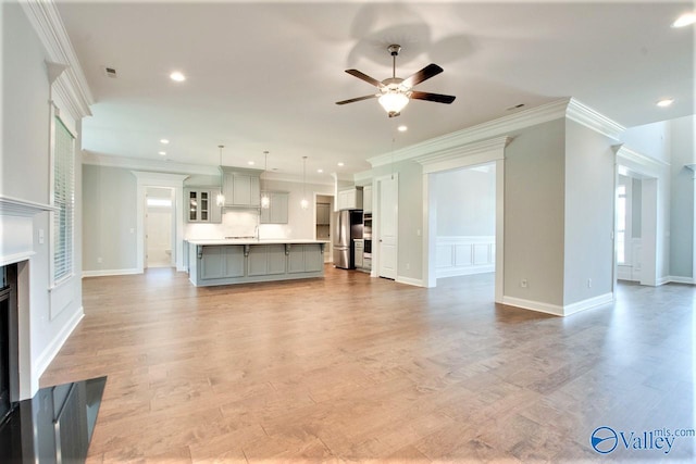 unfurnished living room with crown molding, ceiling fan, and light hardwood / wood-style flooring