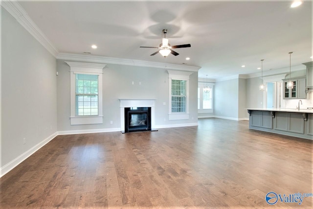 unfurnished living room with ceiling fan with notable chandelier, sink, wood-type flooring, and ornamental molding