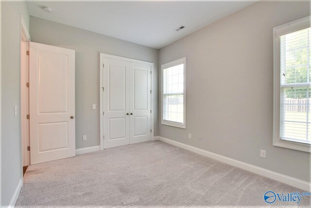 unfurnished bedroom featuring multiple windows, light colored carpet, and a closet