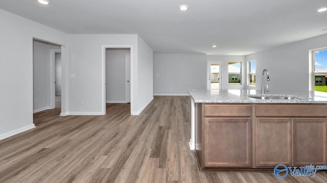 kitchen with a healthy amount of sunlight, wood-type flooring, light stone countertops, and sink