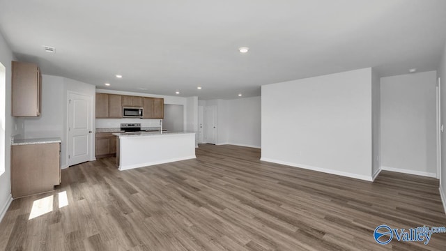 kitchen with sink, stainless steel appliances, dark wood-type flooring, and an island with sink