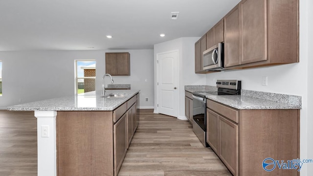 kitchen with a center island with sink, sink, light hardwood / wood-style floors, light stone counters, and stainless steel appliances