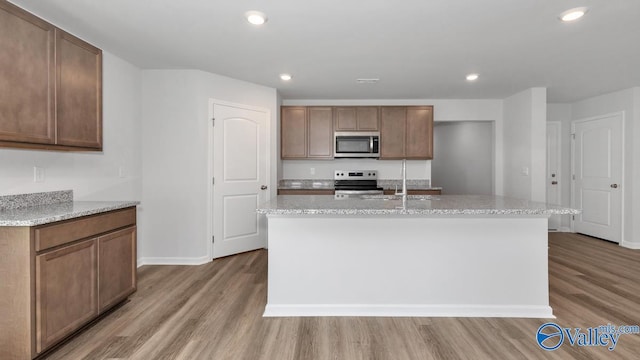 kitchen featuring light stone counters, wood-type flooring, stainless steel appliances, and a kitchen island with sink