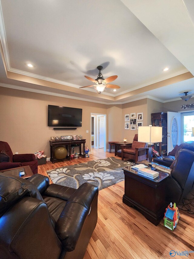 living room featuring hardwood / wood-style floors, ceiling fan, ornamental molding, and a tray ceiling