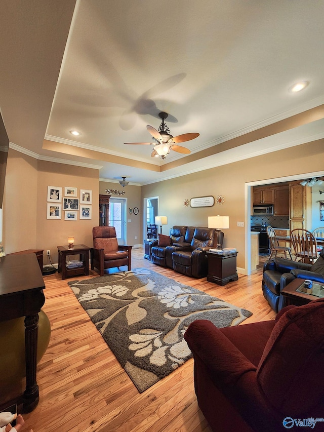 living room featuring ceiling fan, ornamental molding, a tray ceiling, and light hardwood / wood-style flooring