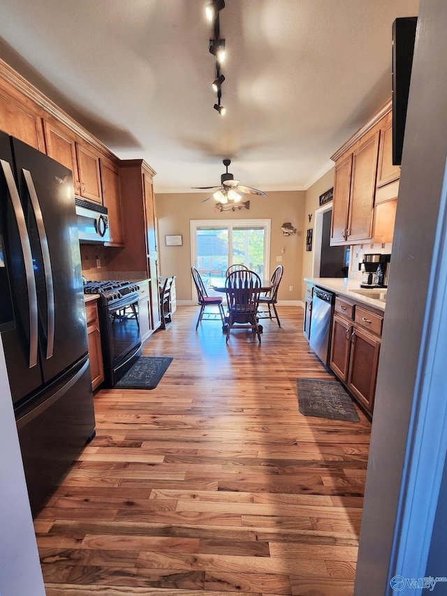 kitchen with track lighting, ceiling fan, crown molding, black appliances, and wood-type flooring