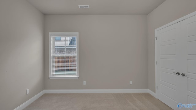 unfurnished room featuring baseboards, light colored carpet, and visible vents