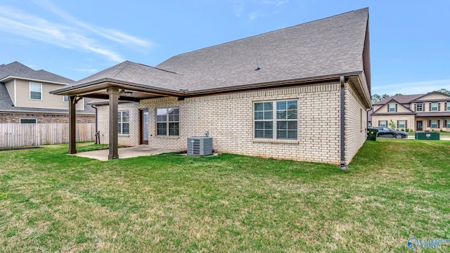rear view of property with fence, brick siding, central AC unit, a patio, and a yard