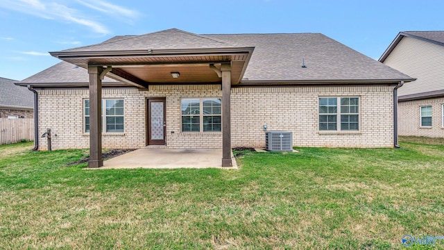 back of property with a lawn, a patio area, central air condition unit, brick siding, and a shingled roof
