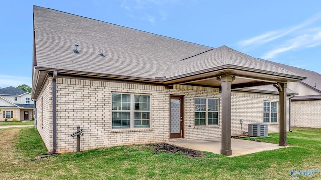 rear view of property featuring a shingled roof, brick siding, a patio area, central air condition unit, and a yard