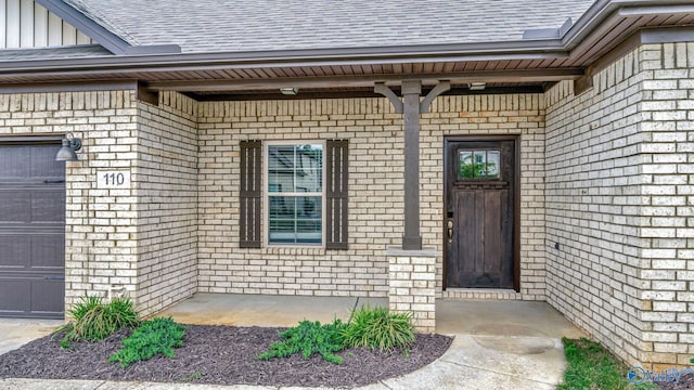 property entrance with board and batten siding, brick siding, roof with shingles, and a garage