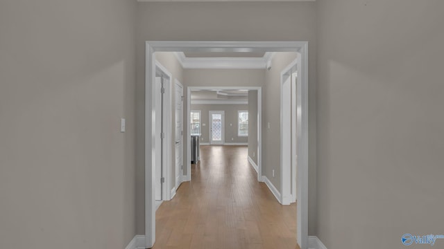 corridor featuring light wood-style floors, ornamental molding, and baseboards