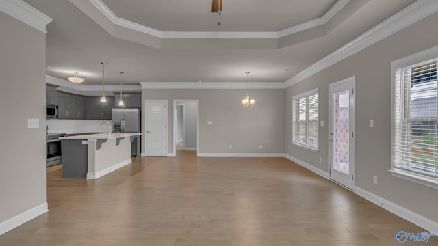 unfurnished living room featuring crown molding, ceiling fan with notable chandelier, a raised ceiling, and light wood-style floors