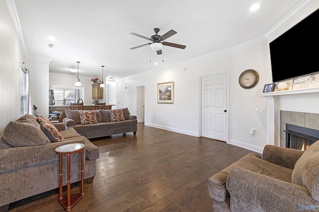 living area featuring a tile fireplace, baseboards, ceiling fan, ornamental molding, and dark wood-type flooring