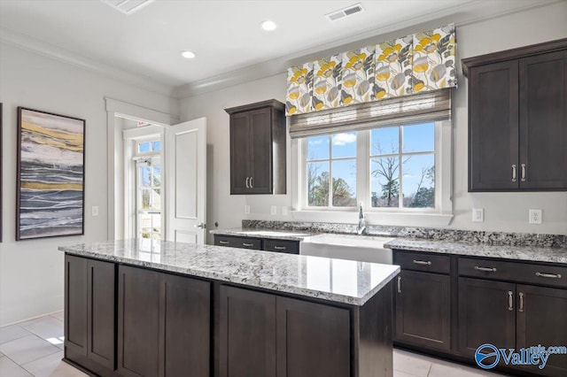 kitchen with ornamental molding, light stone counters, light tile patterned floors, sink, and a center island