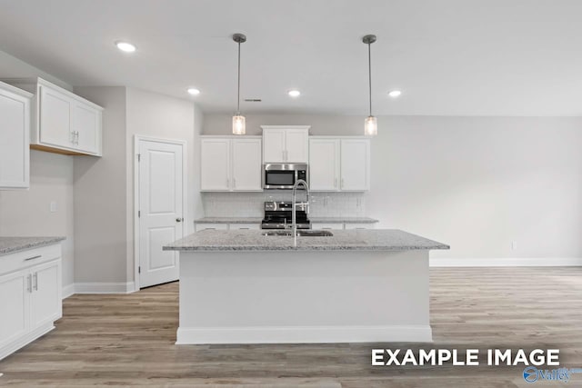 kitchen featuring white cabinets, hanging light fixtures, a kitchen island with sink, and appliances with stainless steel finishes