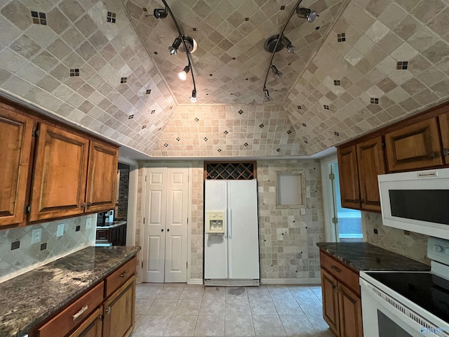 kitchen with tasteful backsplash, dark stone counters, white appliances, and brown cabinets