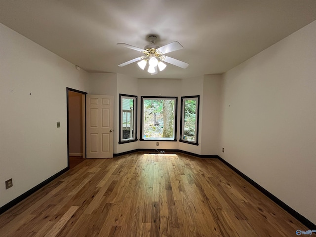 unfurnished room with ceiling fan, wood finished floors, and baseboards