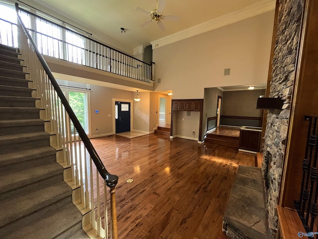 unfurnished living room with a towering ceiling, baseboards, ornamental molding, and dark wood-style flooring