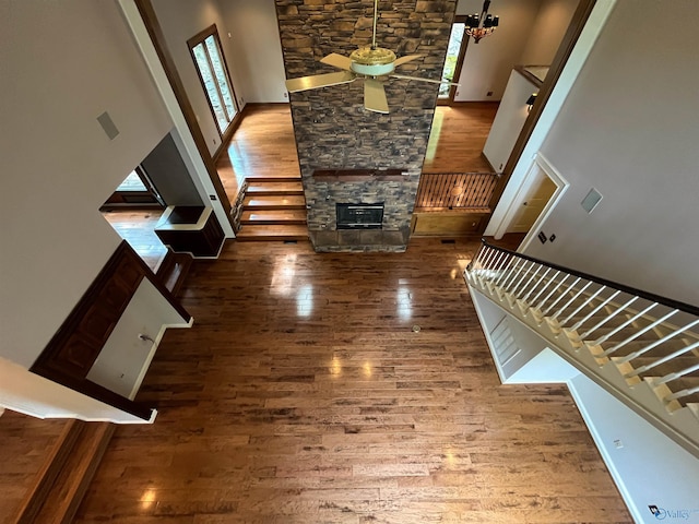 unfurnished living room with a stone fireplace, stairway, a towering ceiling, and wood finished floors