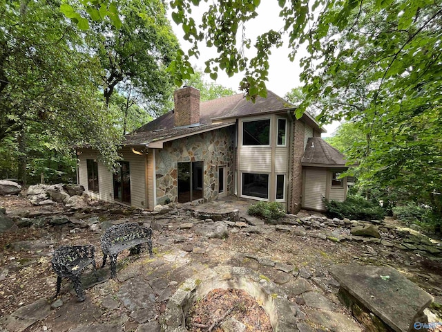 rear view of property with stone siding, a patio, and a chimney