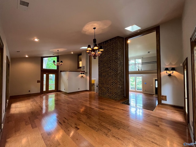 unfurnished living room featuring a chandelier, wood finished floors, a towering ceiling, and baseboards