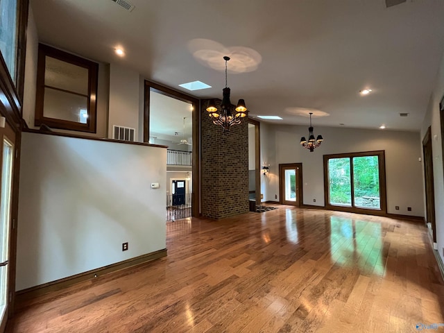 unfurnished living room featuring high vaulted ceiling, a notable chandelier, wood finished floors, visible vents, and baseboards