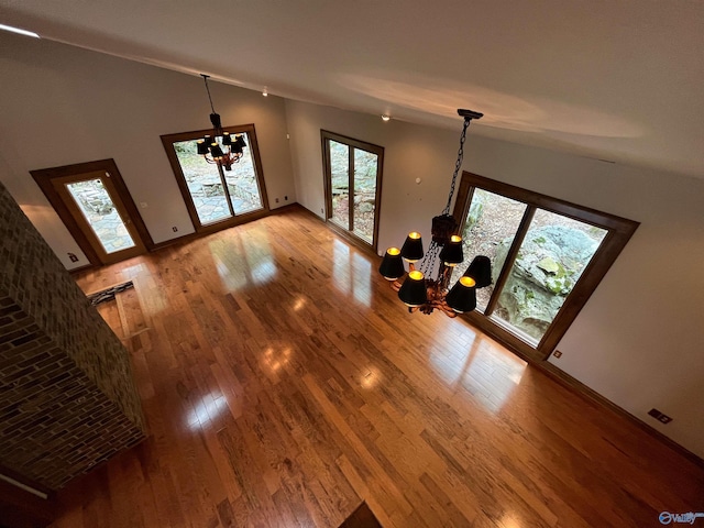 unfurnished living room featuring a chandelier, light wood finished floors, vaulted ceiling, and baseboards