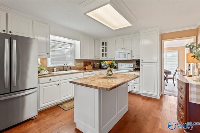 kitchen featuring white appliances, a kitchen island, light wood-style flooring, a sink, and white cabinets