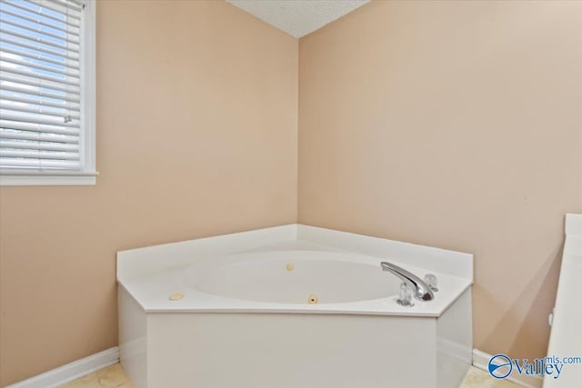 full bathroom featuring tile patterned flooring, a bath, baseboards, and a textured ceiling