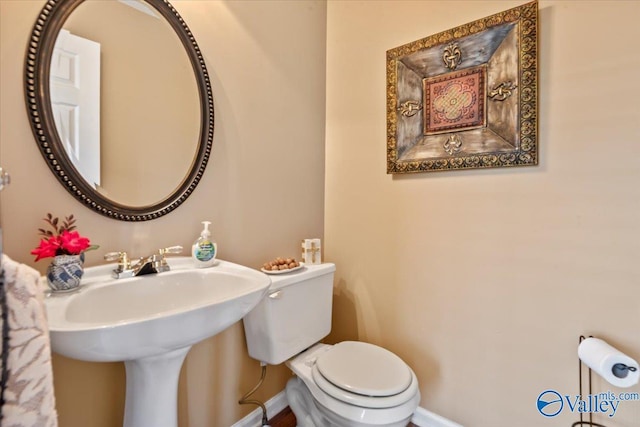 bathroom featuring toilet, baseboards, and a sink