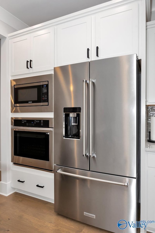 kitchen with stainless steel appliances, white cabinetry, and wood finished floors