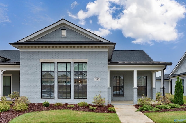 view of front facade featuring brick siding, a shingled roof, and covered porch