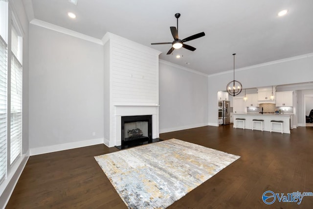 living room featuring baseboards, dark wood-style flooring, ceiling fan with notable chandelier, and crown molding