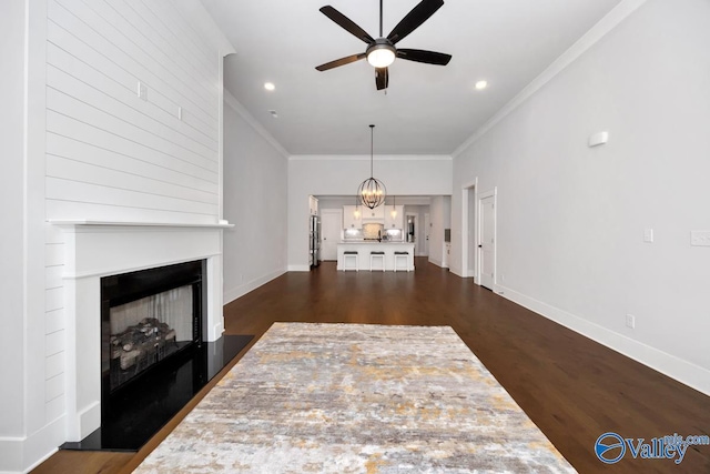 unfurnished living room with a fireplace with raised hearth, dark wood-style flooring, ceiling fan with notable chandelier, and crown molding
