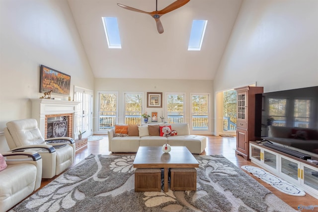 living room with ceiling fan, a high ceiling, a skylight, and light wood-type flooring