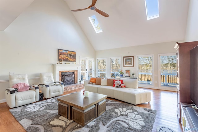 living room with light wood-type flooring, ceiling fan, a skylight, and high vaulted ceiling