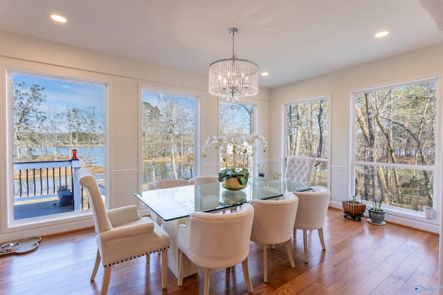 dining area featuring a water view, a wealth of natural light, an inviting chandelier, and hardwood / wood-style floors