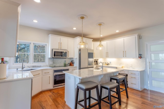 kitchen featuring a center island with sink, appliances with stainless steel finishes, tasteful backsplash, white cabinets, and sink