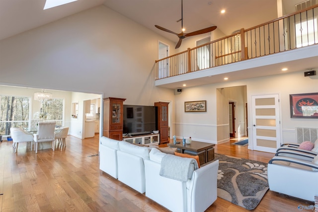 living room with light wood-type flooring, ceiling fan with notable chandelier, and a towering ceiling