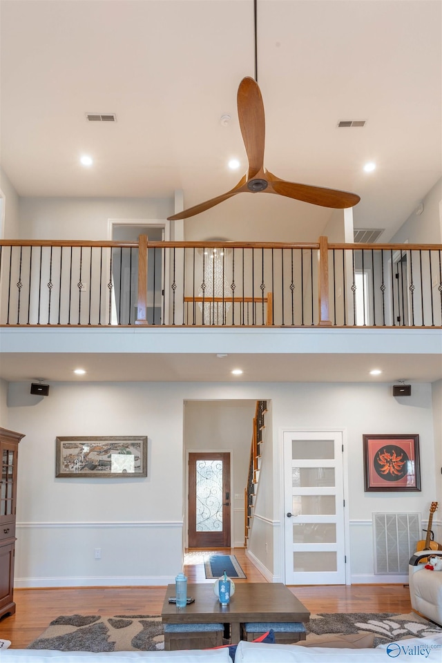 living room with light hardwood / wood-style floors, ceiling fan, and a towering ceiling