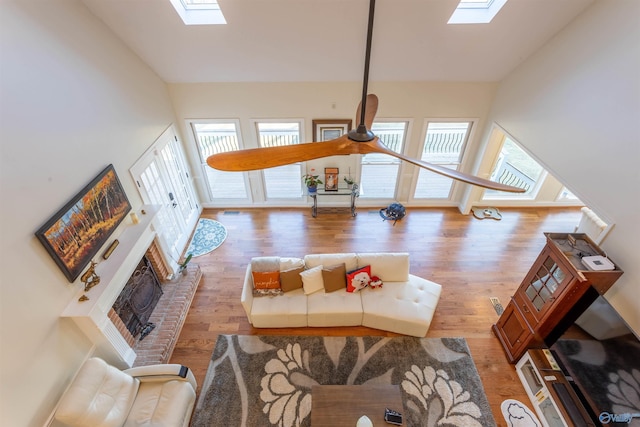 living room with a skylight, a brick fireplace, a high ceiling, and hardwood / wood-style flooring