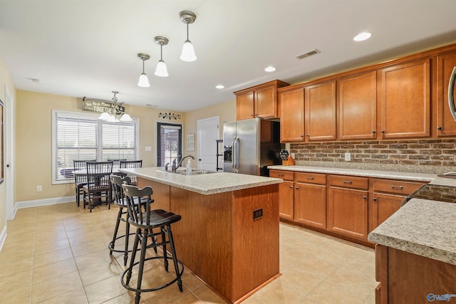 kitchen featuring a kitchen island with sink, sink, stainless steel refrigerator with ice dispenser, decorative backsplash, and decorative light fixtures