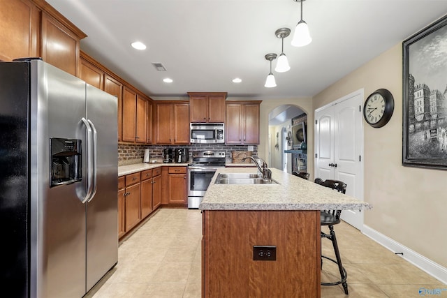 kitchen featuring pendant lighting, sink, backsplash, appliances with stainless steel finishes, and a kitchen bar