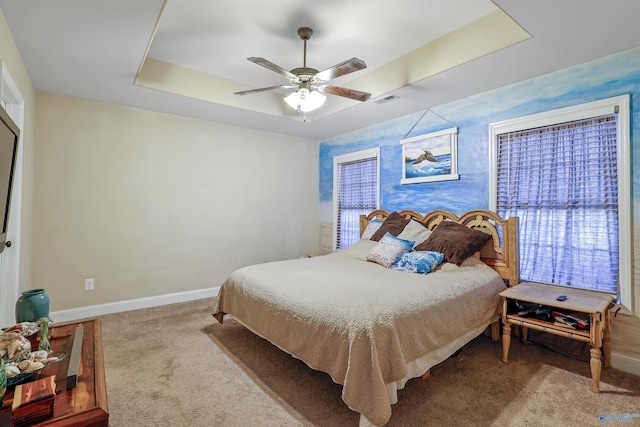 carpeted bedroom with visible vents, baseboards, a raised ceiling, and ceiling fan