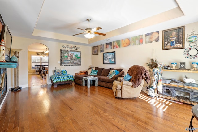 living room with arched walkways, hardwood / wood-style flooring, a tray ceiling, and ceiling fan
