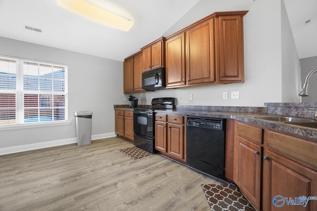 kitchen featuring lofted ceiling, light wood-type flooring, black appliances, and sink