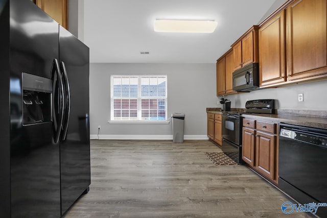 kitchen with light wood-type flooring, black appliances, and dark stone counters