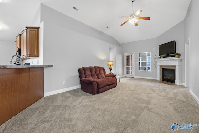 carpeted living room with ceiling fan, a tile fireplace, and vaulted ceiling